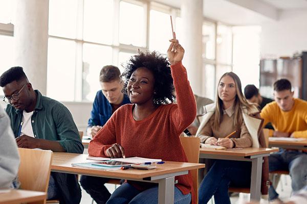 Smiling college student raises her hand in a full classroom